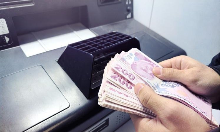 A person counting 200 TL banknotes in front of an ATM